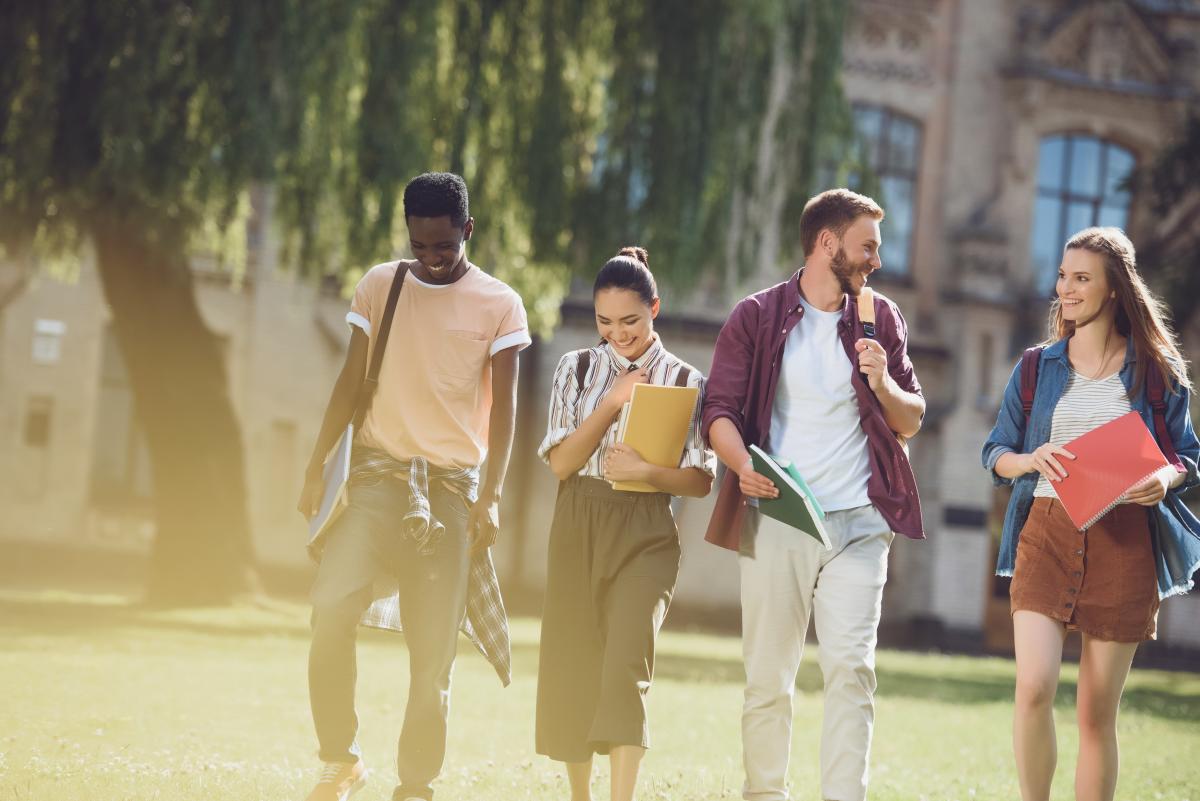 Eine Gruppe von vier jungen diversen Studierenden, die über den Uni-Campus spazieren